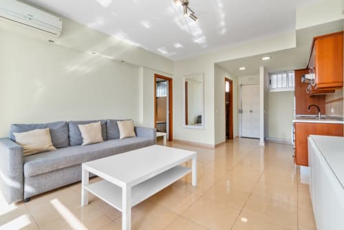 Modernes Wohnzimmer mit grauem Sofa, weißem Couchtisch, Küche und orangefarbenen Schränken in Maspalomas, Gran Canaria