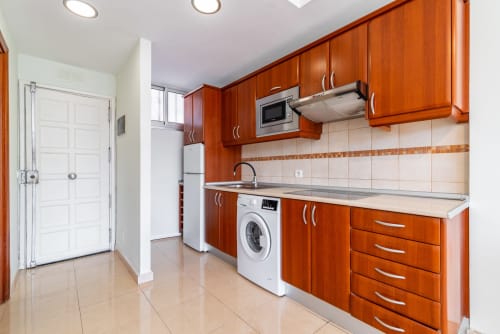 Moderne Küche mit Holzschränken, Edelstahlgeräten und weißer Fliesenrückwand in der Wohnung in Maspalomas