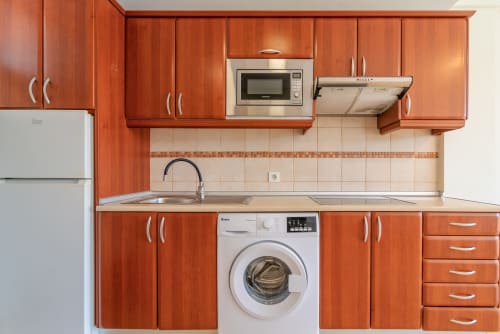 Moderne Küche mit rot-orangen Schränken, Mikrowelle, Waschmaschine und Edelstahlgeräten im HomeStay Gran Canaria