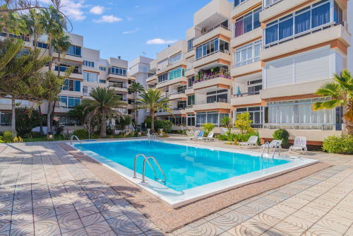 Strahlend blauer Swimmingpool mit Palmen und mehrstöckigen Apartmentgebäuden im Home Stay Gran Canaria, Maspalomas