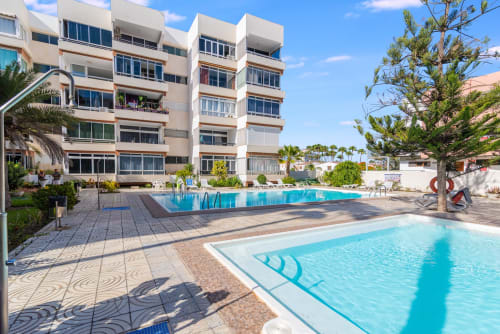 Poolbereich des Maspalomas-Resorts mit modernem Apartmentgebäude, zwei Swimmingpools, Palmen und sonniger Terrasse im Home Stay