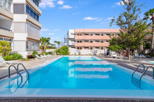 Kristallklarer Swimmingpool im HomeStay Gran Canaria in Maspalomas mit modernen Apartmenthäusern, Palmen und Sonnenschein