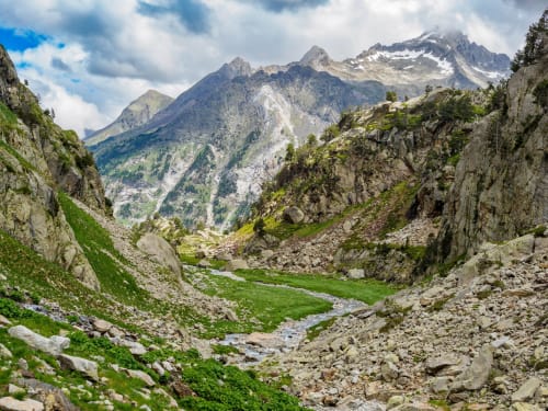 Alpine valley with rocky peaks, green meadows, and stream near Hotel Fonsispa in Renanué