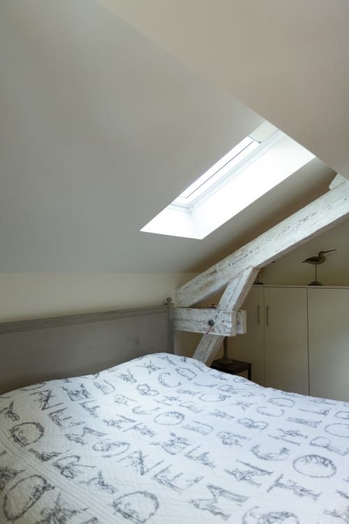 Chambre lumineuse sous les toits à la Gare Godillot B&B à Saint-Ouen-sur-Seine avec lucarne et poutres en bois blanc.