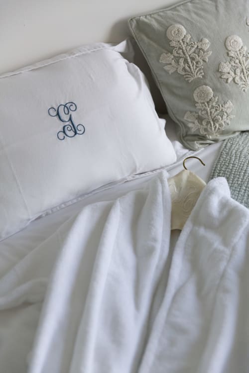 Oreiller monogrammé blanc et coussins brodés sur le lit de l'appartement Gare Godillot, Saint-Ouen-sur-Seine