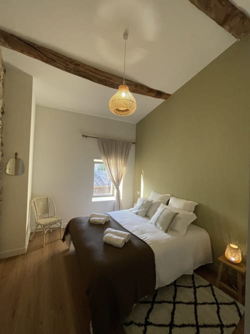 Chambre douillette au Domaine Maison Girardon avec murs vert sauge, luminaire pendant tissé et poutres en bois