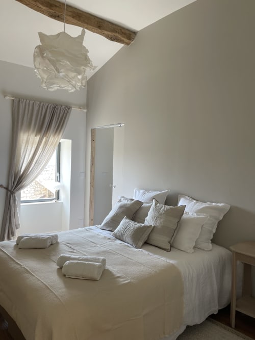 Chambre lumineuse au Domaine Maison Girardon avec literie blanche, oreillers, serviettes roulées, suspension et poutre en bois