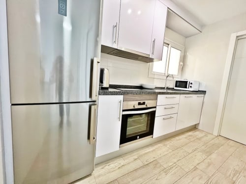 Cocina moderna con electrodomésticos de acero inoxidable, muebles blancos y suelo efecto madera en apartamento frente al mar en Fuengirola
