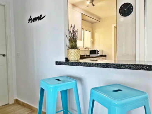 Cocina-bar luminosa frente al mar con taburetes turquesas, espejo, planta de lavanda y decoración moderna en Fuengirola
