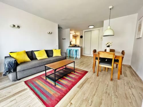 Moderno apartamento frente al mar en Fuengirola con luminosa sala de estar, detalles en amarillo, mesa de comedor y decoración costera
