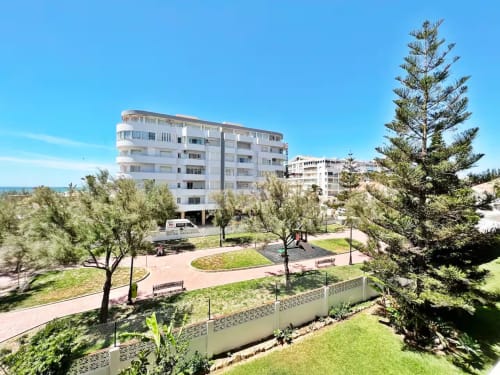 Complejo de apartamentos frente a playa en Fuengirola con edificios modernos blancos, jardines verdes y cielo azul despejado
