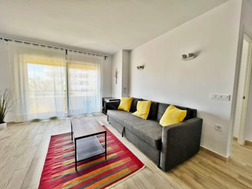 Luminoso salón de apartamento frente al mar en Fuengirola con sofá gris, cojines amarillos y alfombra multicolor