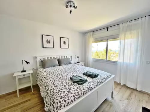 Luminoso dormitorio de apartamento frente al mar en Fuengirola con mobiliario blanco, ropa de cama estampada y vistas al mar