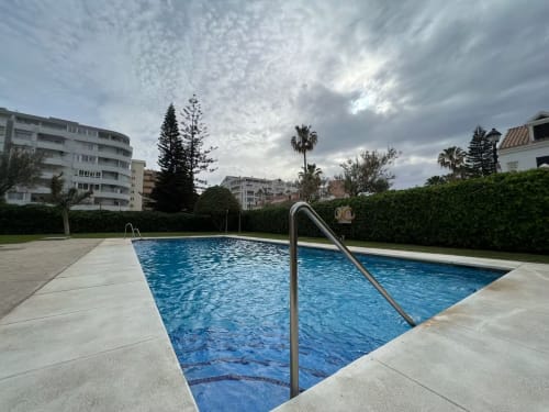 Piscina comunitaria en residencial frente al mar en Fuengirola, rodeada de palmeras y edificios modernos
