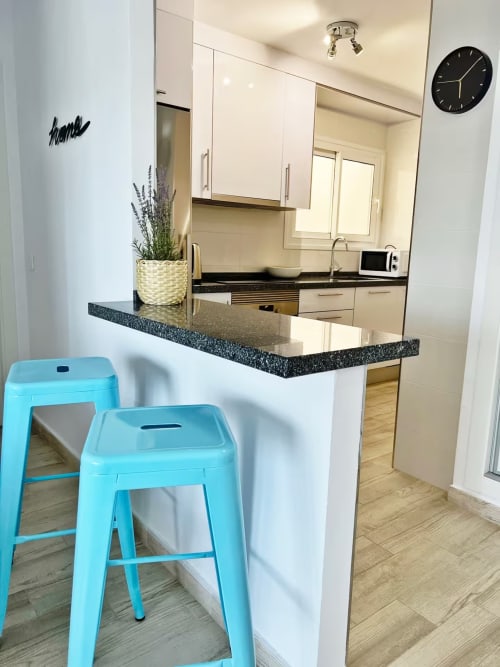 Moderna cocina luminosa con isla, encimeras negras, taburetes turquesas y muebles blancos en primera línea de playa, Fuengirola