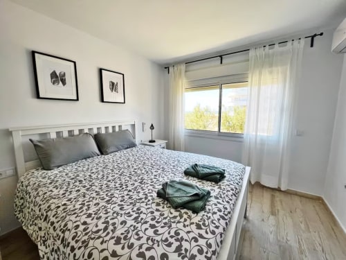 Luminoso dormitorio de apartamento frente al mar en Fuengirola con cama blanca moderna, ropa de cama estampada y vistas al mar