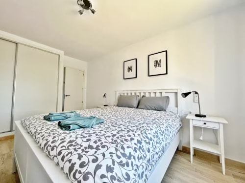 Luminoso dormitorio en apartamento frente al mar en Fuengirola con ropa de cama estampada, muebles blancos y decoración minimalista