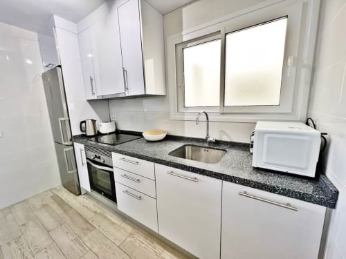 Cocina moderna con muebles blancos, encimera de granito y electrodomésticos de acero inoxidable en apartamento frente al mar, Fuengirola