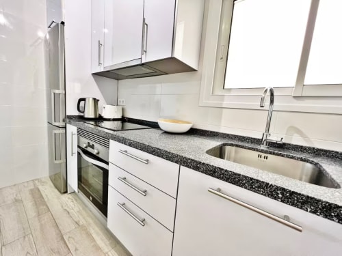 Cocina moderna con muebles blancos, encimeras de granito negro y electrodomésticos de acero inoxidable en apartamento frente al mar de Fuengirola