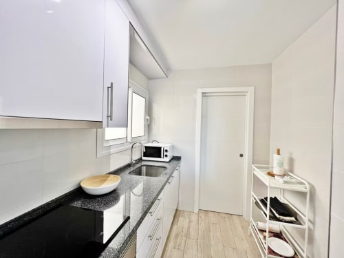 Moderna cocina luminosa con encimera de granito, armarios blancos y suelo tipo madera en apartamento frente al mar de Fuengirola