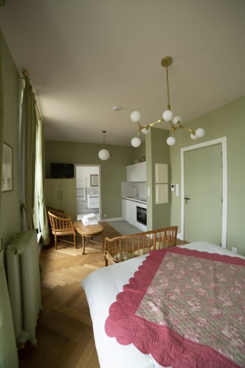 Chambre moderne à la Gare Godillot B&B à Saint-Ouen avec murs vert sauge, luminaires suspendus en laiton, mobilier en bois et