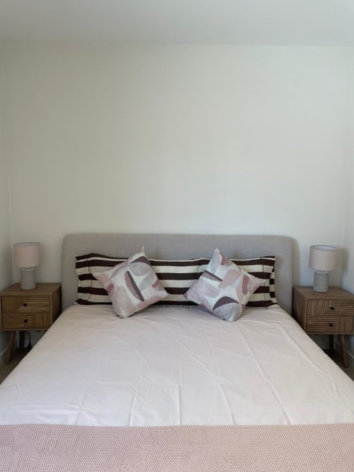 Quarto moderno em Vila Sotto Mayor com cabeceira estofada cinza, almofadas listradas, roupa de cama branca e mesinhas de madeira