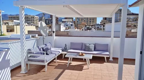 Soleada terraza ático en Fuengirola con pérgola blanca, tumbonas rayadas, sofá gris y vistas a la ciudad en Ático del sol