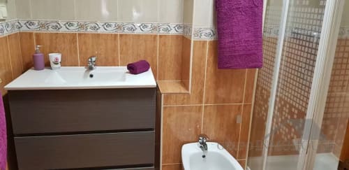 Baño moderno con azulejos efecto madera, doble lavabo y toallas moradas en el Ático del sol, Fuengirola