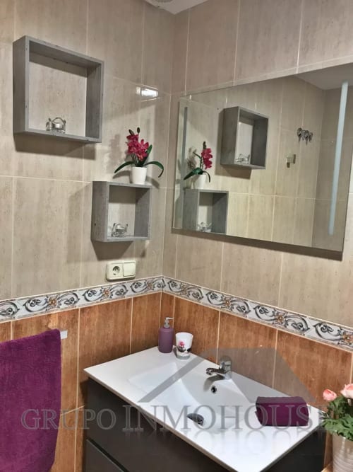 Baño moderno en apartamento Ático del sol de Grupo Inmo House Fuengirola con lavabo blanco, azulejos beige y detalles en madera