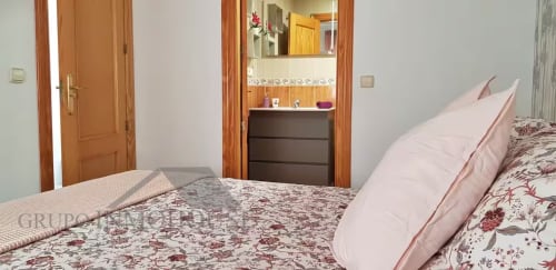 Amplio dormitorio en apartamento Ático del sol de Grupo Inmo House, Fuengirola, con ropa de cama floral y muebles de madera
