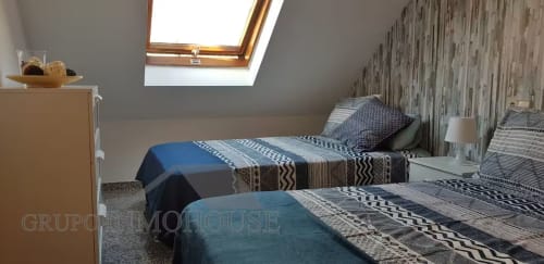 Luminoso dormitorio abuhardillado en Fuengirola con camas gemelas, ropa de cama estampada, claraboya y mobiliario moderno en Grupo Inmo House
