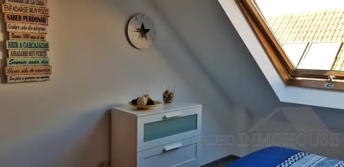 Dormitorio luminoso en buhardilla de Ático del Sol en Fuengirola con tragaluz, reloj de pared, cómoda blanca y decoración motivacional española