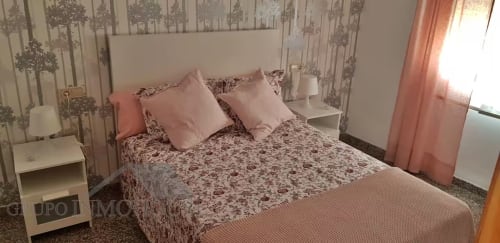 Dormitorio Ático del Sol en apartamento de Fuengirola con ropa de cama floral, almohadas rosas, papel pintado con motivos de árboles y cortinas translúcidas