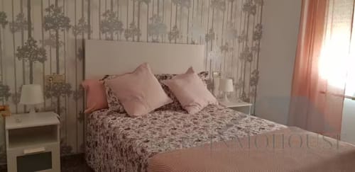 Dormitorio luminoso en apartamento Ático del sol en Fuengirola con ropa de cama estampada, almohadas rosas, papel tapiz de árboles y luz natural