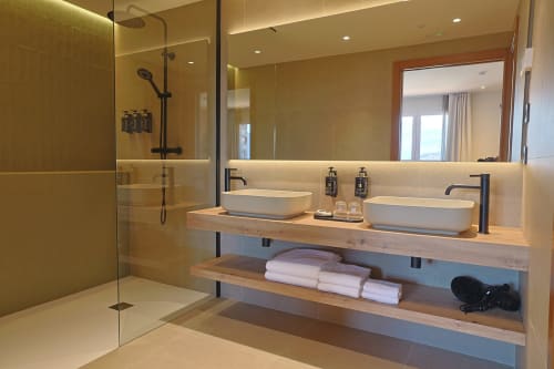 Baño moderno del Hotel Fonsispa con doble lavabo, ducha a ras de suelo y repisa de madera con toallas