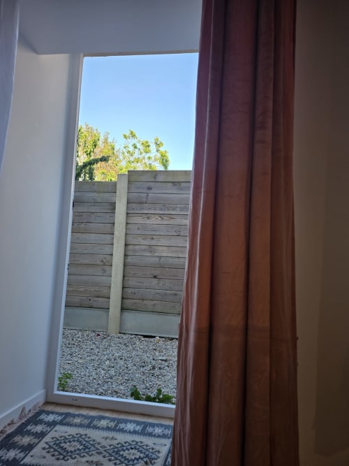 Chambre Villa Kahlo : Baie vitrée aux rideaux bordeaux donnant sur clôture bois et jardin à Colleville-sur-Mer