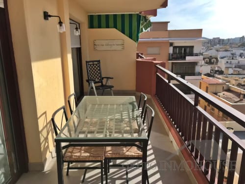 Soleada terraza de apartamento frente al mar en Fuengirola con mesa de comedor, sillas y vistas a los edificios costeros mediterráneos