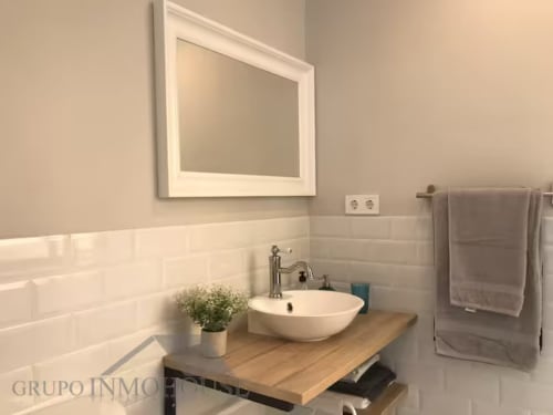 Baño moderno en apartamento de Fuengirola con azulejos blancos tipo metro, lavamanos de cerámica y encimera de madera
