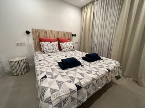 Habitación de apartamento frente al mar en Fuengirola con ropa de cama geométrica, almohadas rojas y vistas a la ciudad y océano