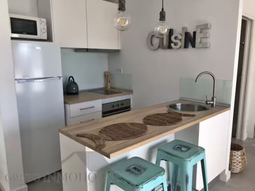 Cocina de apartamento frente al mar en Fuengirola con muebles blancos, encimeras de madera y taburetes turquesas
