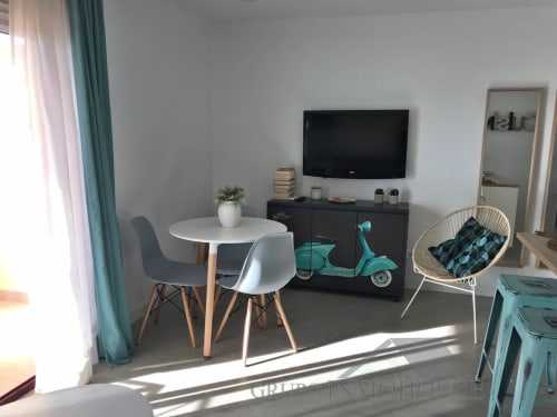 Salón moderno en Fuengirola con mesa de comedor blanca, mueble TV negro, decoración de scooter turquesa y vistas a la ciudad