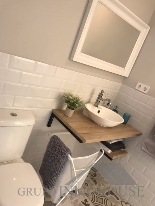Baño moderno con azulejos blancos tipo metro, tocador de madera, planta en maceta y armario espejado en apartamento de Fuengirola