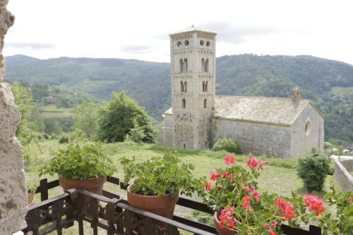 Torre de iglesia medieval con vistas al valle de Molló desde el balcón de Casa Tapiolas con plantas en flor