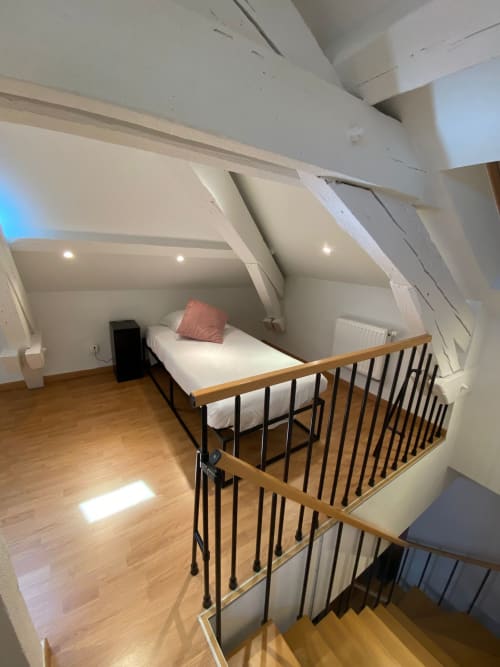 Chambre mezzanine dans l'appartement de Belfort avec murs blancs, lit en bois, garde-corps métalliques et fenêtres de toit.