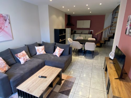 Salon ouvert moderne à l'Hôtel Saint Christophe avec canapé gris, table à manger, cuisine et escaliers à Belfort