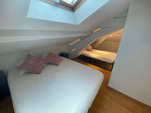 Chambre mansardée douillette à l'Hôtel Saint Christophe Belfort avec literie blanche, oreillers bordeaux, lucarne et parquet.