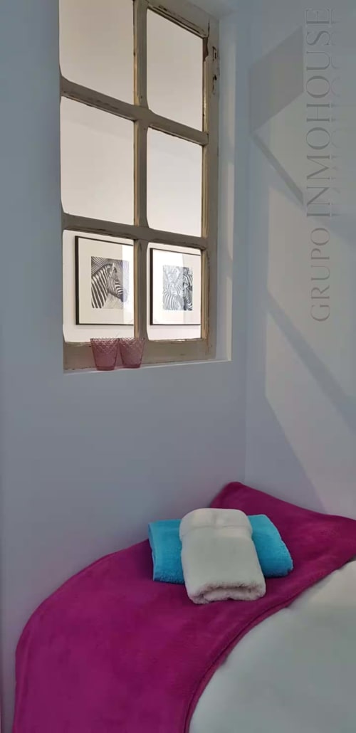 Acogedor rincón dormitorio en apartamento de Fuengirola con ventana, obra de arte de cebra y ropa de cama magenta