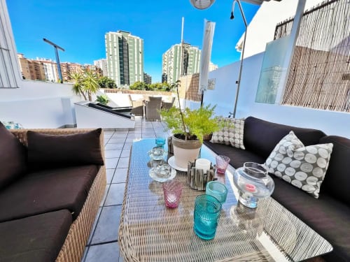 Terraza en azotea con sofás negros, plantas y vistas de la ciudad en apartamento de Fuengirola