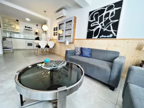 Salón moderno de apartamento en Fuengirola con sofá gris, mesa de cristal redonda y cocina abierta