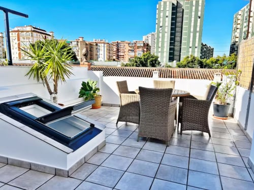 Soleada terraza en la azotea del apartamento de Fuengirola con mobiliario de mimbre, vistas a la ciudad y tragaluces modernos